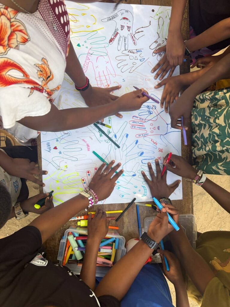 Mani di bambini e volontari che disegnano su un grande foglio