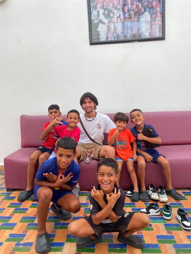 Un volontario seduto su un divano insieme a sei bambini sorridenti