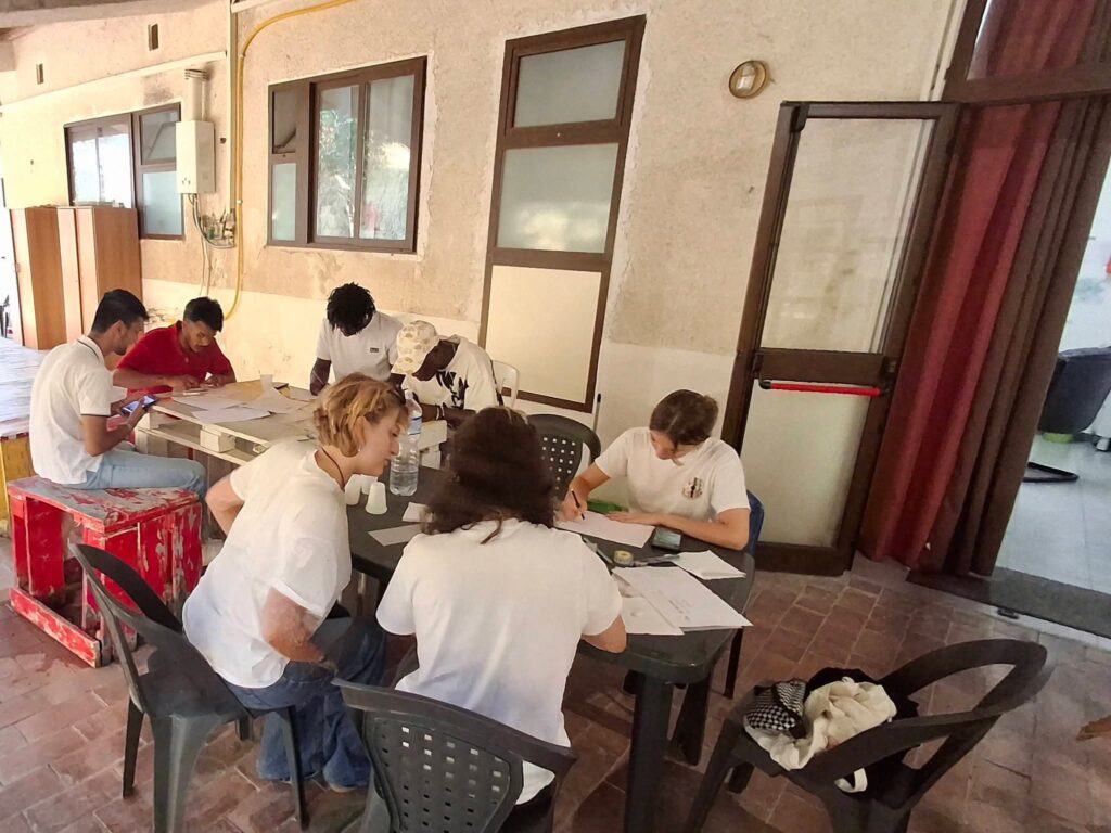Ragazzi e volontarie al lavoro ai tavoli sotto una veranda