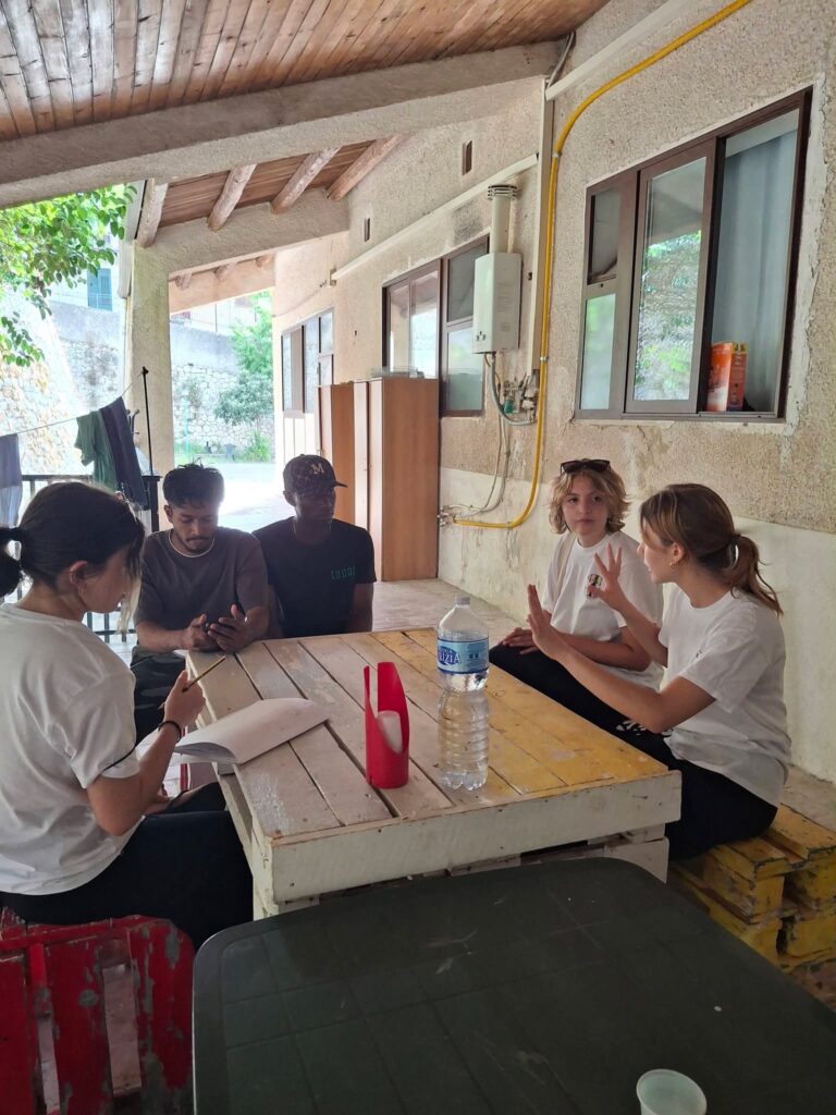 Ragazzi e volontarie al lavoro ai tavoli sotto una veranda