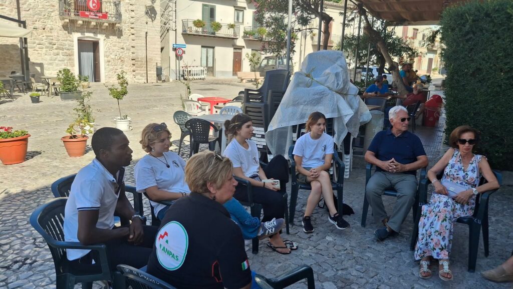 Volontarie e abitanti seduti in cerchio in una piazza
