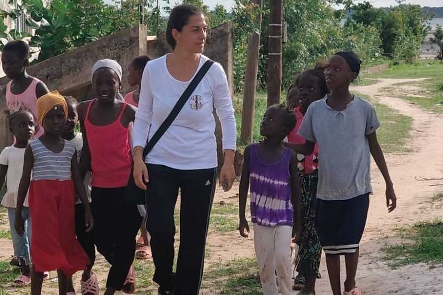 Una volontaria cammina lungo una strada di terra con un gruppo di bambini