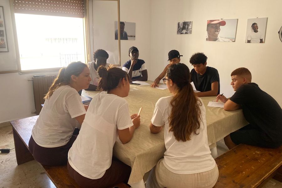 Volontarie e ragazzi al lavoro attorno a un tavolo durante un laboratorio
