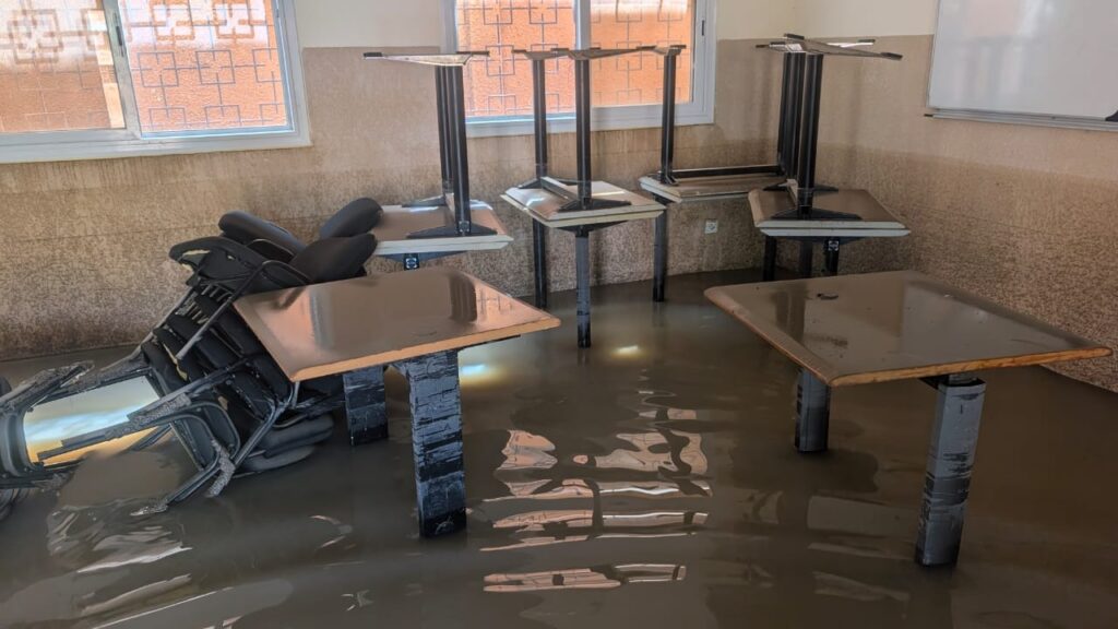 Un'aula allagata, con banchi e sedie rovesciati nell'acqua